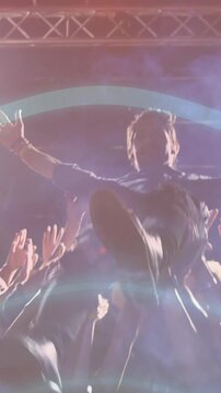 Vertical video: Performer reaching out, crowd lifting him off stage engaging fans under music beams