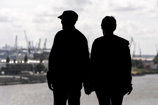 At the Hamburg port the harbor industry logistics and shipping meet the waterfront as silhouettes of people pass cranes in working docks