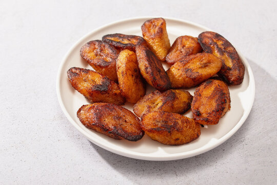 Fried sweet plantain tajadas on white plate, light background.