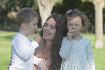 Fototapeta premium Mother and her kids share a happy moment together in a park having a snack, capturing natural bonding and connection in a summer outdoor portrait