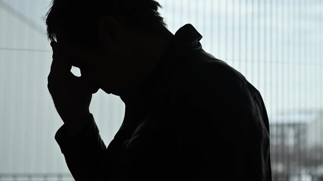 Silhouette of a distressed man rethinking and contemplating by the window, 4K