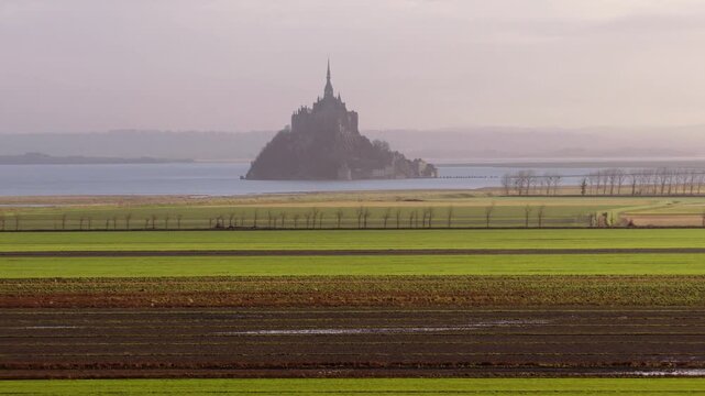 Aerial view of the historic Mont Saint-Michel abbey rising above the horizon with green agricultural fields in the foreground Mont Saint-Michel, Normandy, France.