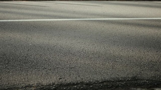 Close view of asphalt road with white lane marking as vehicle passes along roadway