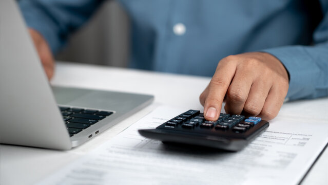 Financial advisors analyze business reports and expenses at the office desk, review accounting records, assets, balance sheets, stock market statistics, and annual tax laws to protect the business.