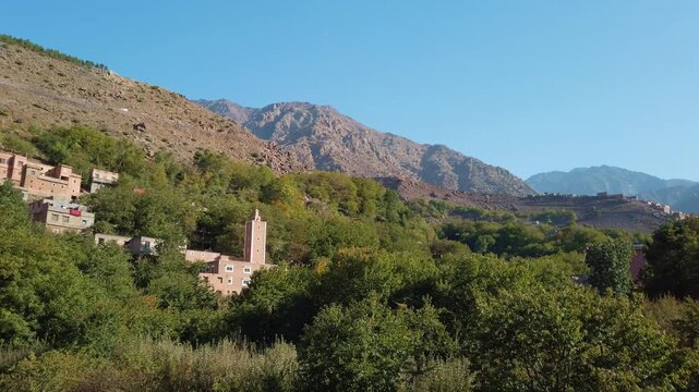 Imlil, a Berber mountain village in Morocco&rsquo;s High Atlas Mountains near Toubkal National Park, features traditional architecture amid rocky hillsides, and clear blue sky in an elevated panoramic view.