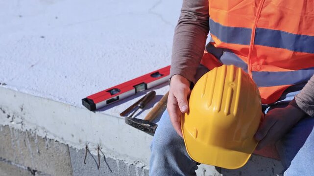 Construction worker working outdoors on a construction site, making a pause and holding a yellow hardhat.