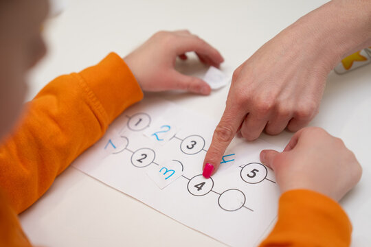 Close-up of a child and woman completing a number sequencing worksheet