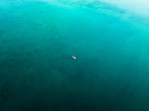 Aerial view of a solitary boat adrift on an endless expanse of turquoise, where the ocean's depths meet the sky's embrace, Noumea, New Caledonia.
