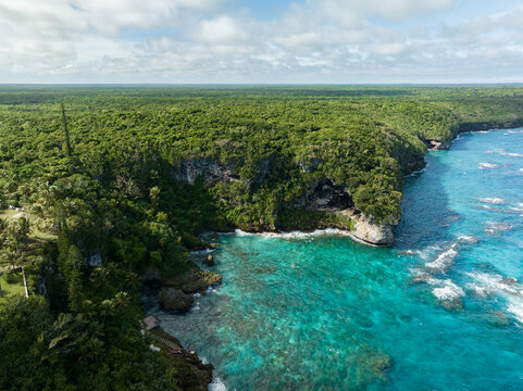 Aerial view of the vibrant turquoise sea meeting the rugged, verdant cliffs of the coastline, a tropical paradise from above, Joking, Lifou, New Caledonia.