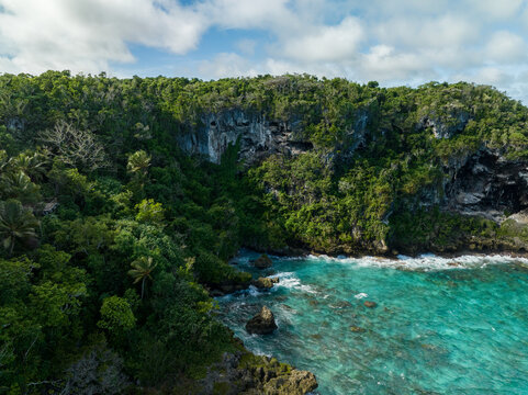 Aerial view of turquoise waters meet the rugged coastline, vibrant green foliage blankets the cliffs, Joking, Lifou, New Caledonia.