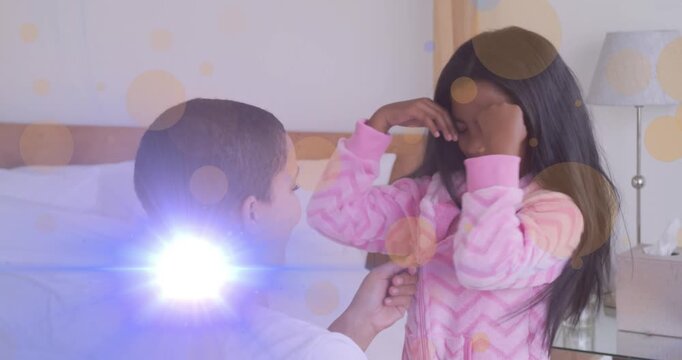Animation of light moving over happy african american mother and daughter putting on pyjama