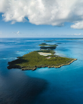 Aerial view of a vibrant, verdant island surrounded by turquoise waters, where the depths transition from light blues to deep indigos, Ouvea, Loyalty Islands Province, New Caledonia.