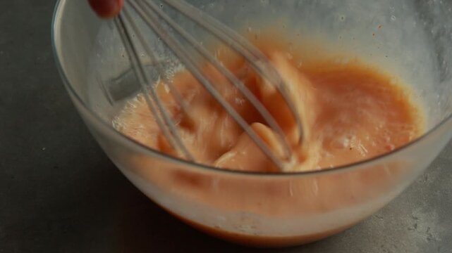 Close-up of whisking eggs, milk, and spices in a glass bowl to prepare a frittata or omelet, natural light