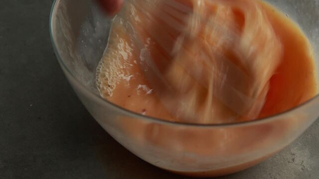 Close-up of whisking eggs, milk, and spices in a glass bowl to prepare a frittata or omelet, natural light