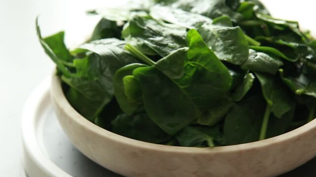Close-up of fresh, raw baby spinach leaves in a white ceramic bowl, natural light