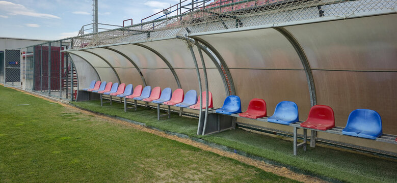 Colorful Team Bench And Dugout Seats Alongside A Grass Sports Field At A Small Stadium