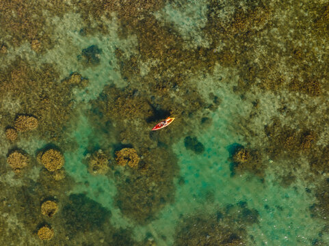 Aerial view of a solitary kayak glides across the cerulean waters, weaving through the submerged landscapes of coral reefs, Goro, New Caledonia.