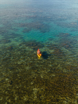 Aerial view of a lone kayaker in a yellow boat glides over the crystal-clear turquoise waters, revealing the intricate tapestry of the coral reef below, Goro, South Province, New Caledonia.
