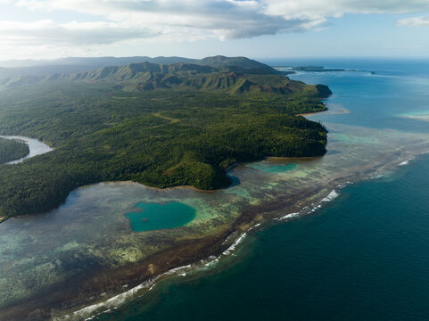 Aerial view of the vibrant coastline where the deep blue ocean meets the lush green forests and winding rivers, Goro, South Province, New Caledonia.