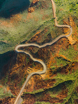 Aerial view of a winding road cutting through a landscape of contrasting earthy tones and verdant vegetation, a dance of nature and human design, Goro, South Province, New Caledonia.