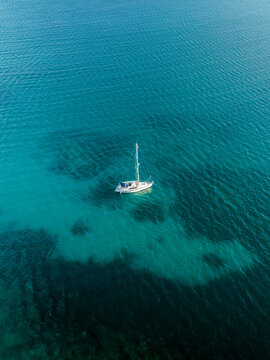 Aerial view of a lone white sailboat adrift on the shimmering turquoise waters, casting a dark shadow on the seabed below, Goro, South Province, New Caledonia.