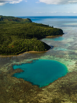 Aerial view of turquoise waters meet lush greenery, a vibrant contrast against the backdrop of the clear blue ocean horizon, Goro, South Province, New Caledonia.