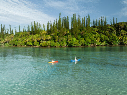 Aerial view of two kayakers glide across the turquoise waters, framed by lush, emerald green vegetation, Goro, South Province, New Caledonia.
