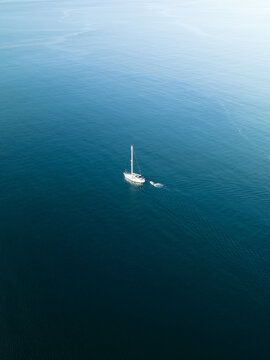 Aerial view of a lone sailboat adrift in the vast, deep blue expanse, its white sails contrasting against the dark waters, Goro, South Province, New Caledonia.