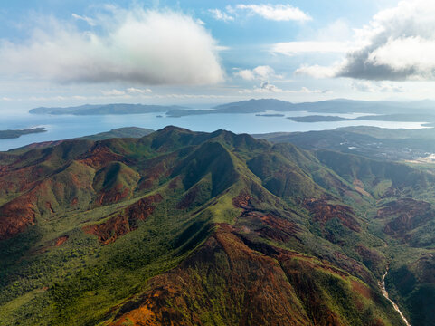 Aerial view of vibrant green and red mountains contrasting with the serene blue waters surrounding the islands, Goro, South Province, New Caledonia.
