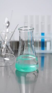 Scientist conducting chemical experiment by mixing green reagent into a liquid solution inside a glass flask in a laboratory