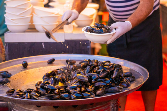 View of a chef serving steaming mussels from a large metal dish, a culinary symphony of colors and aromas, in Pula, Istria County, Croatia.