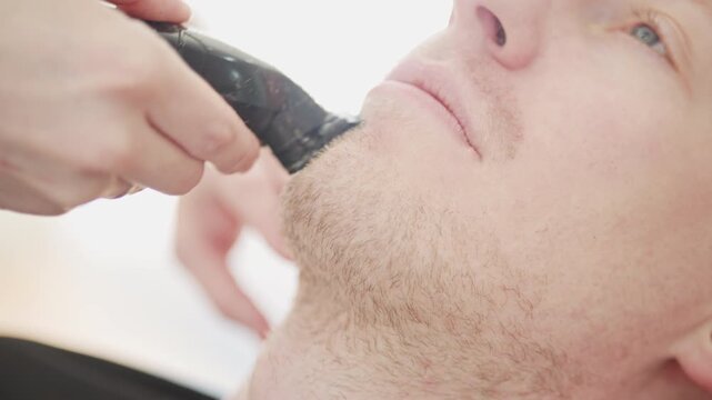 Professional barber shaving man's beard with electric trimmer