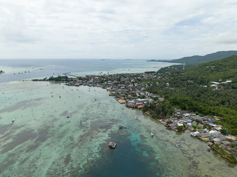 Aerial view of a vibrant coastal settlement where turquoise waters meet lush greenery, creating a stunning contrast under the open sky, Karimunjawa, Central Java, Indonesia.