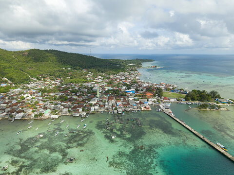 Aerial view of the vibrant coastal village where cerulean waters meet the lush green hills, Karimunjawa, Central Java, Indonesia.