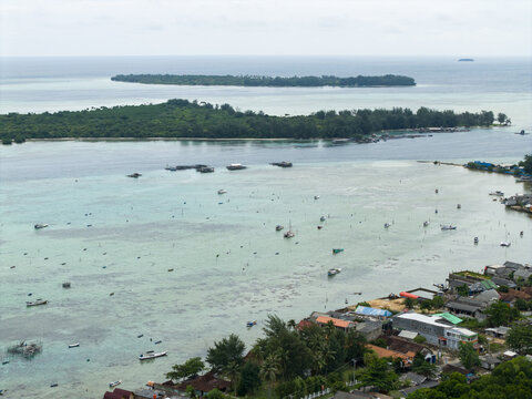 Aerial view of boats dot the turquoise waters near the shore, contrasting with the lush green islands in the distance, Karimunjawa, Central Java, Indonesia.