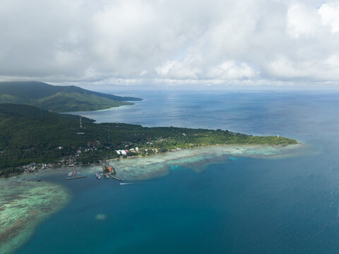 Aerial view of the island's lush greenery meeting the turquoise sea, a coastal village nestled along the shore, Karimunjawa, Central Java, Indonesia.
