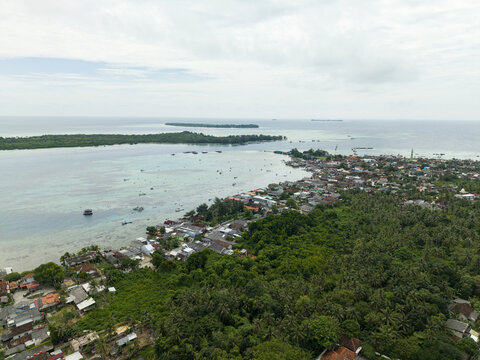 Aerial view of a vibrant coastal town where emerald forests meet the turquoise sea, contrasting with the terracotta rooftops, Karimunjawa, Central Java, Indonesia.
