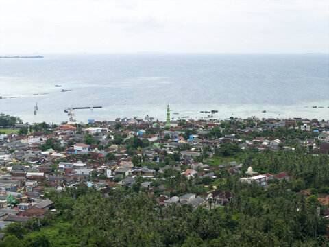Aerial view of houses and trees stretching to the ocean with a mosque standing prominently, Karimunjawa, Central Java, Indonesia.