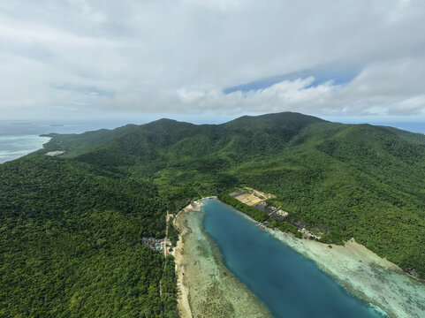 Aerial view of a vibrant turquoise lagoon snaking inland, embraced by dense green forests under a vast sky, Karimunjawa, Central Java, Indonesia.