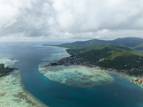 Aerial view of the coastline meets the turquoise sea near the town with lush mountains in the distance, Karimunjawa, Central Java, Indonesia.