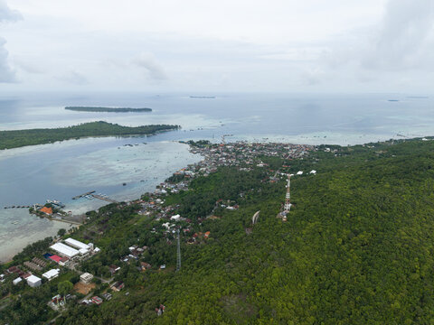 Aerial view of a coastal town nestled between lush green hills and turquoise waters, Karimunjawa, Central Java, Indonesia.