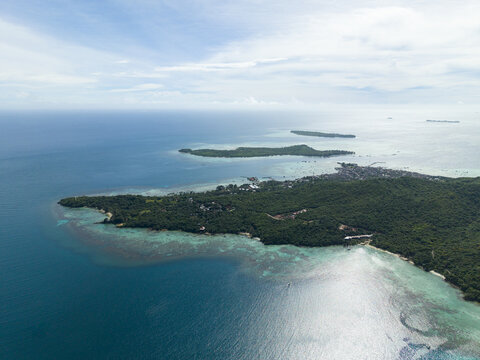 Aerial view of a vibrant island fringed with turquoise waters meeting the deep blue sea under a soft sky, Karimunjawa, Central Java, Indonesia.