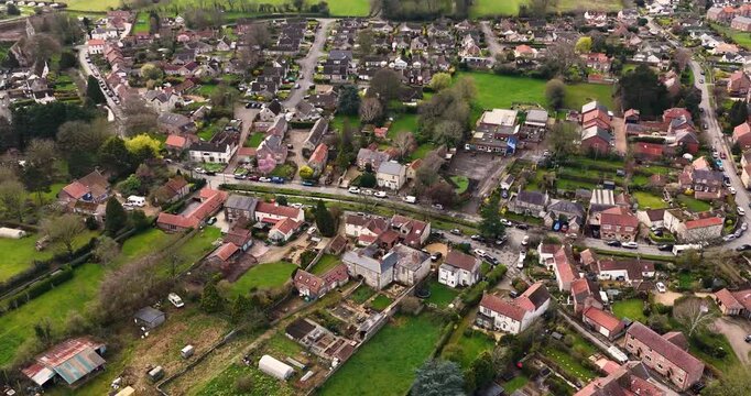 Aerial drone footage of the village of Bishop Monkton street with houses gardens parked cars and visible school keep clear road marking beside a narrow water channel in a rural village setting
