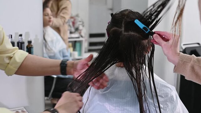 Hairdresser applies anti-hair loss treatment growth stimulant in beauty salon. Professional hair care. Hair mask, coloring, keratin treatment with four hands, all hairstylists working simultaneously