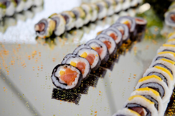 Assorted sushi rolls on a reflective silver tray. Elegant catering display with fresh maki and uramaki for a luxury event or wedding. © Vincenzo Rampolla