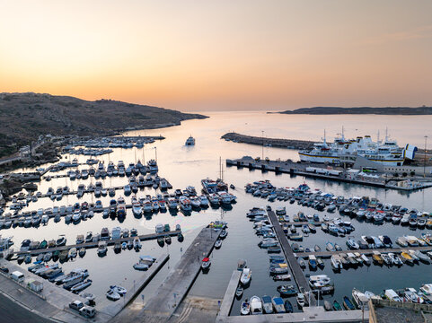 Aerial view of the Mgarr Harbour where the boats rest on the calm waters, framed by the rugged coastline, Mgarr Harbour, Gozo, Malta.