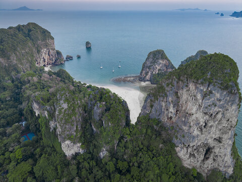 Aerial view of dramatic limestone cliffs cloaked in lush greenery meet a pristine white sand beach and turquoise waters, Krabi, Thailand.