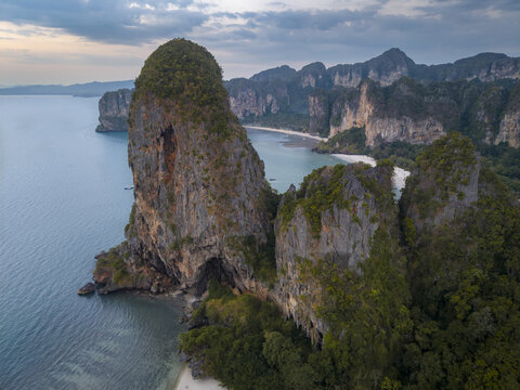 Aerial view of striking limestone cliffs and lush vegetation meet turquoise waters under a serene sky at Railay Beach, Krabi, Thailand.