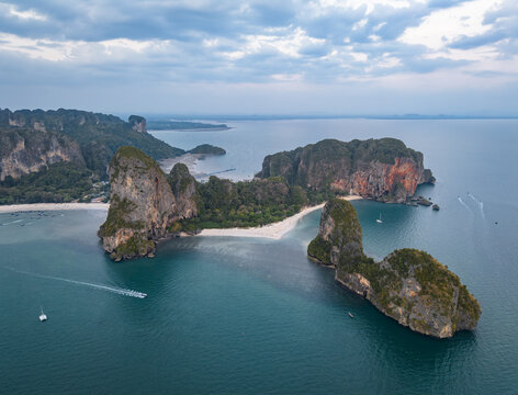 Aerial view of towering limestone cliffs meet the turquoise sea, fringed by white sands and lush greenery, Krabi, Thailand.