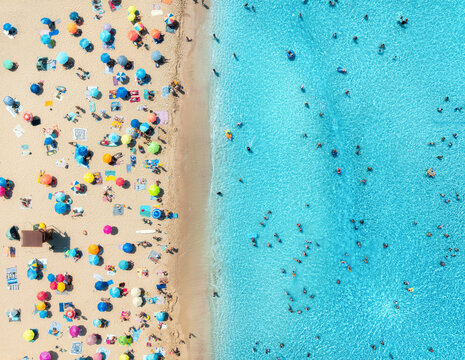 Aerial drone view of colorful umbrellas on sandy beach, swimming people in blue sea on sunny summer day. Top down view. Mallorca, Balearic Islands, Spain. Tropical. Clear turquoise water. Travel
